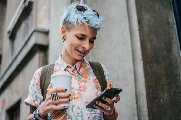 A young punk woman holding paper coffee cup and her mobile phone
