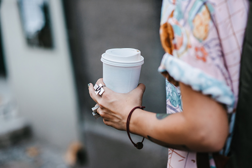Close-up of a young person walking and holding the paper coffee cup