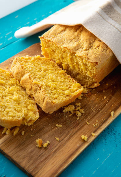 istock Cornbread is bread containing cornmeal, corn flour. Beautiful homemade yellow sliced cornbread loaf under cotton towel. Blue wood background. Above view. 1313995688
