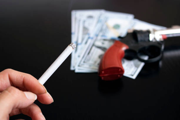 Gun, dollars and hand with cigarette on wooden table