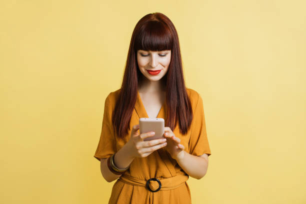 istock Using mobile phone, typing sms message. People and technologies. Smiling young woman in yellow overalls posing isolated on pastel yellow background and using smartphone 1313997631