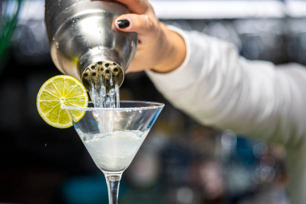 pouring cocktail into glass with lemon slice - transparent holding glass focus on foreground imagens e fotografias de stock