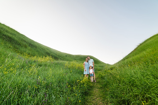 The daughter hugging parents on nature. Mom, dad, and girl walk in the grass. Happy young family spending time together, outside, on vacation, outdoors. The concept of a family holiday.