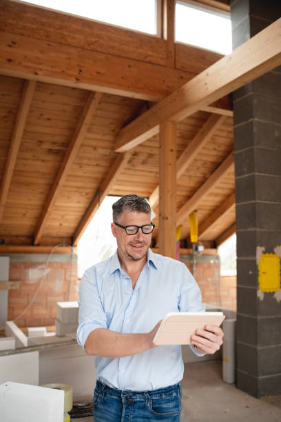 arquitecto masculino con gafas negras se encuentra en la obra en la casa loft y sostiene su tableta - construction worker architect construction manual worker fotografías e imágenes de stock