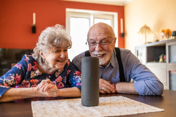 couples aînés excités utilisant un assistant virtuel à la maison - senior couple audio photos et images de collection