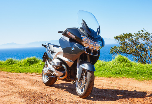 Cape Town, South Africa - September 16, 2011: A large luxury touring motorcycle, a BMW R1200RT, stands parked beside the ocean on a dirt road near Simon's Town on a bright sunny day.