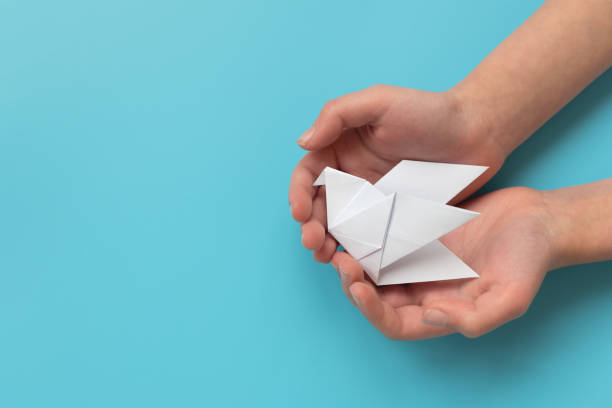 Child hands holding white paper dove on blue background
