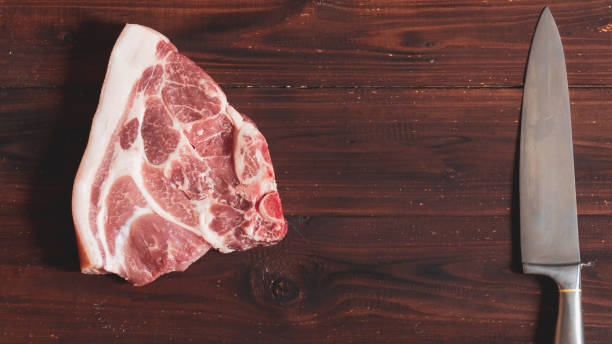 a piece of raw pork meat and a large knife on a brown wooden background - top sirloin imagens e fotografias de stock