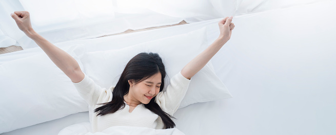 attractive Beautiful young asian woman sleeping while lying in her bed and relaxing comfortably. stretching wake up for work or the day off. Concept of pleasant and rest reinstatement for active life.