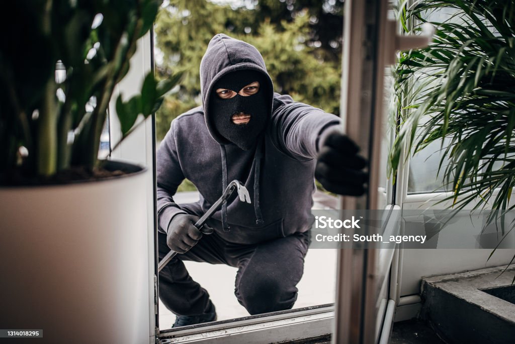 Robber breaking in house One man, criminal dressed all in black with crowbar, breaking in through window in house. Thief Stock Photo