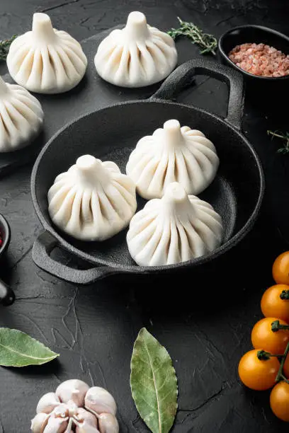 Photo of Uzbek Manti. Manti or manty dumplings, popular uzbek-asian dish, in frying cast iron pan, on black stone background