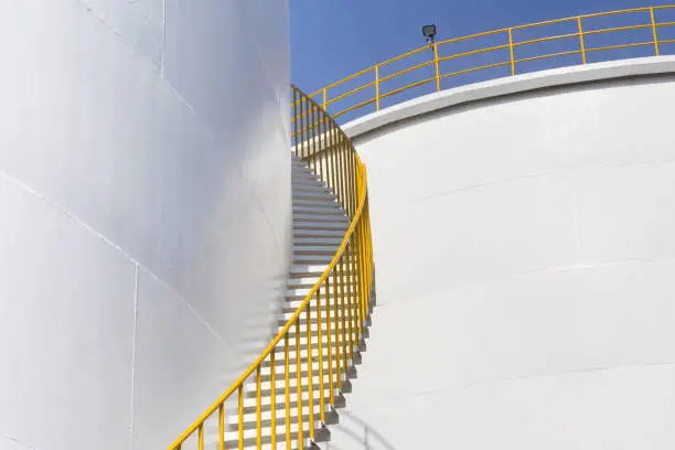 Photo of white fuel tanks against blue sky, white steel petroleum silo and white steel stair with yellow metal handrail.