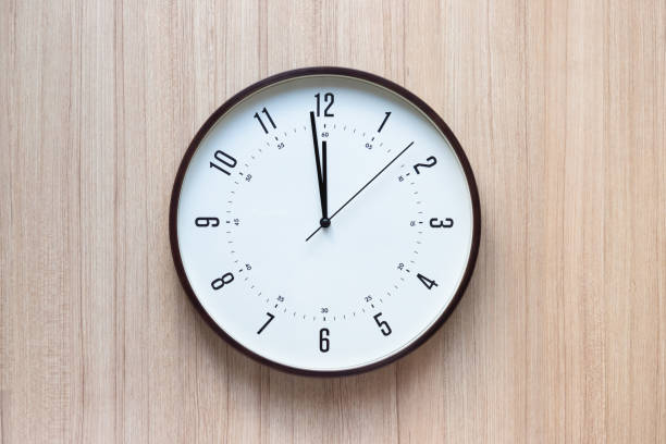 istock brown plastic clock on light wooden wall. show time in midday. concept : time for appointment or having lunch. 1314022398
