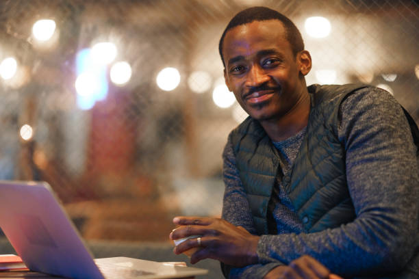istock Portrait of black ethnicity man looking at camera and smiling while using laptop and relaxing outside of cafe at night 1314023788