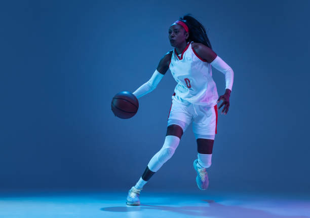 hermosa jugadora afroamericana de baloncesto en movimiento y acción con luz de neón sobre fondo azul. concepto de estilo de vida saludable, deporte profesional, hobby. - stroboscopic image fotografías e imágenes de stock