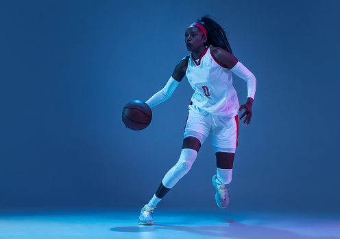 Throwing ball in a jump. Portrait of teen girl in blue uniform training, playing basketball isolated over white background. Concept of sport, active lifestyle, health, team game and ad