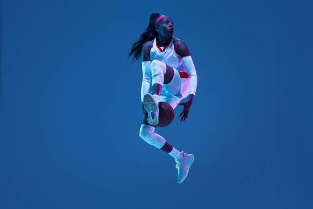 hermosa jugadora afroamericana de baloncesto en movimiento y acción con luz de neón sobre fondo azul. concepto de estilo de vida saludable, deporte profesional, hobby. - stroboscopic image fotografías e imágenes de stock