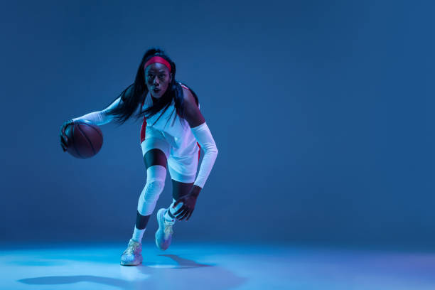 hermosa jugadora afroamericana de baloncesto en movimiento y acción con luz de neón sobre fondo azul. concepto de estilo de vida saludable, deporte profesional, hobby. - stroboscopic image fotografías e imágenes de stock