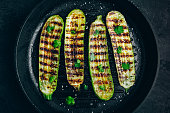 Grilled zucchini slices in cast iron pan on dark stone or concrete background