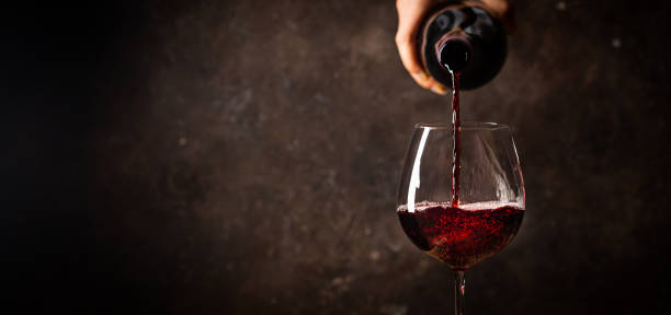 Pouring red wine into the glass Pouring red wine into the glass against rustic dark wooden background maroon stock pictures, royalty-free photos & images