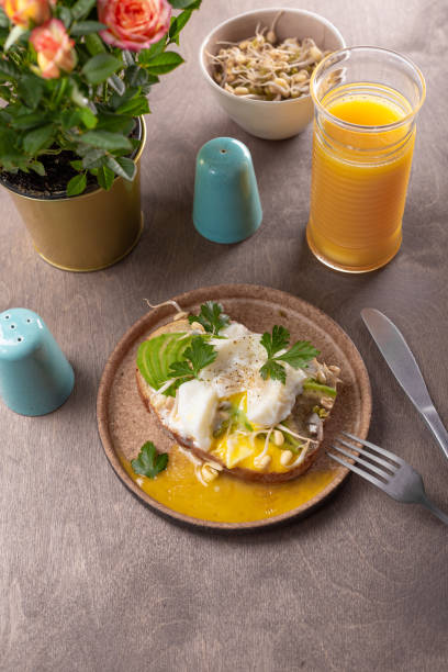 istock Light summer breakfast - sandwich with avocado, cottage cheese, sprouted beans and poached egg with orange juice on the table 1314035184