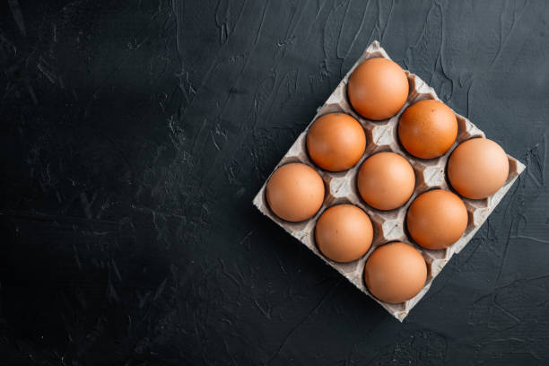 Brown eggs in carton box tray, on black background, top view flat lay , with space for text  copyspace