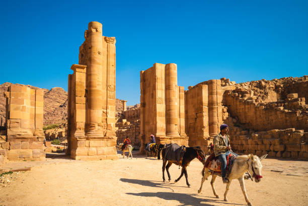 March 22, 2019: A man riding a donkey through the Hadrian Gate ,aka the Temenos Gate, located at the end of the Colonnaded Street in petra, jordan. Donkey riding is a popular way to explore petra.