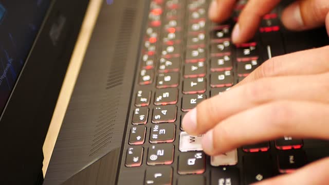Hands on the keyboard play a game. Gaming laptop. close-up. Side view. Hacker. Mans hands typing on a modern trendy keyboard. Cybercrime male hands on keyboard