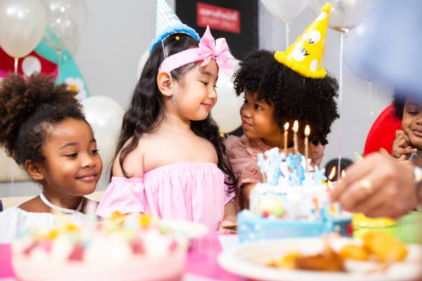 group of little kids in party hat with birthday cake at birthday party. diversity friends in childhood concept - child party group of people little girls imagens e fotografias de stock