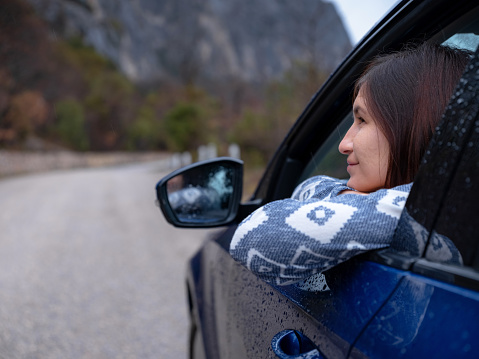 Asian young hipster woman traveling on car vacation. Autumn drive. The rain is falling. The concept of freedom of movement. Fall weekend in the mountains.