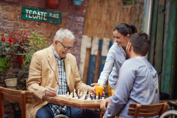istock An elderly man is served by beautiful waitress while he plays a chess with his young friend in the bar. Leisure, bar, friendship, outdoor 1314046564