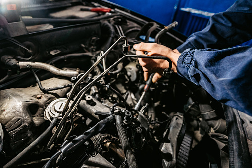 Auto mechanic working on car engine in mechanics garage. Repair service.