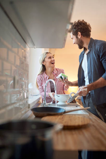 imagen de la pareja de adultos jóvenes divirtiéndose mientras lava platos - equipment housework remote domestic kitchen fotografías e imágenes de stock