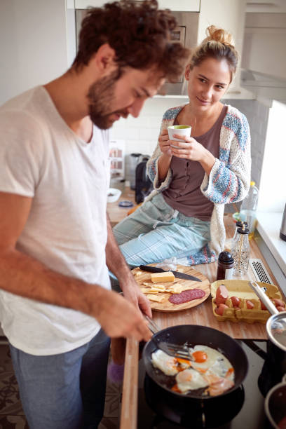 istock beardy young man with curly hair making breakfast, while his female partner looking with love at him 1314055884