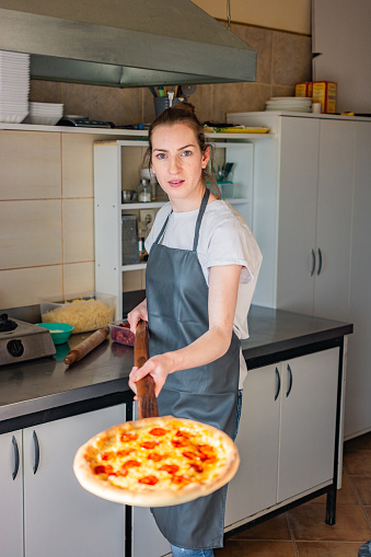 Young female chef holding peel with pizza in the kitchen