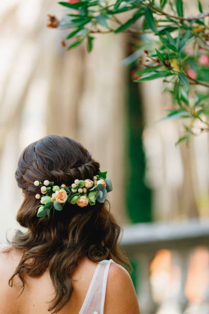 A bride with an adornment of natural flowers in her hair stands under a blooming oleander, back view A bride with an adornment of natural flowers in her hair stands under a blooming oleander, back view . High quality photo bridal hair stock pictures, royalty-free photos & images