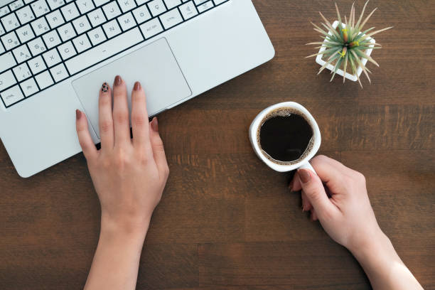 istock female hands are using laptop computer and holding coffee cup. working on wooden table, top view 1314065544