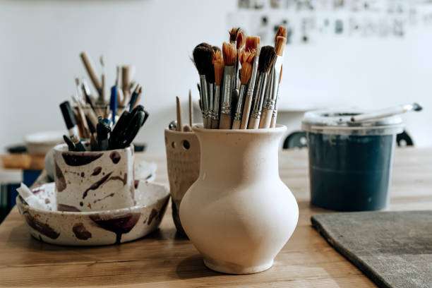 istock Ceramic utensils with brushes and other artisan tools on the table in art studio. Traditional pottery craft. Ceramics workshop concept 1314065640