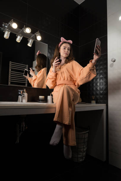 istock Attractive young woman in a bathroom communicating on a smartphone and drinking wine. Relaxation and leisure concept. 1314069528