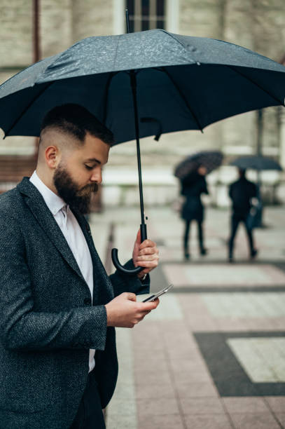 istock Businessman using a smartphone and holding a black umbrella 1314073788