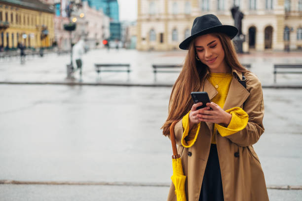 istock Woman using a smartphone and holding a yellow umbrella outside 1314073825