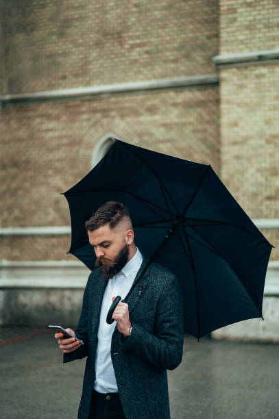 istock Businessman using a smartphone and holding a black umbrella 1314073830