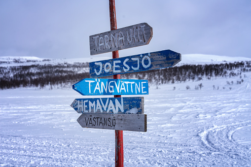 Wooden multi direction signpost to local villages in Lapland mountains for snowmobile tourists. Sunny day, snowy mountains with birch trees on blurry background. Sweden, Joesjo. Close up view