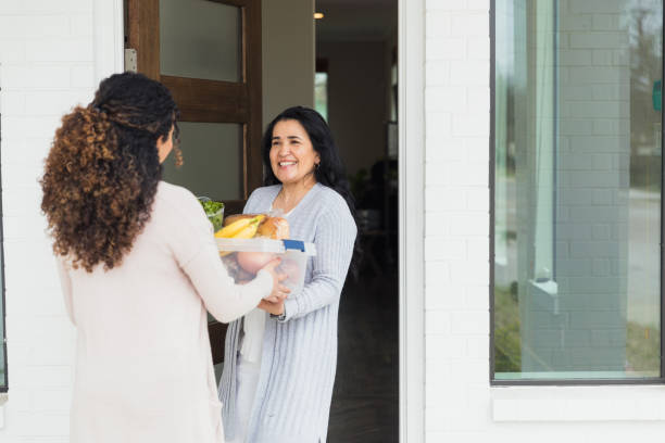 Mid adult daughter brings food to ill mature adult mother The unrecognizable mid adult daughter brings food to her ill mature adult mother. neighbour stock pictures, royalty-free photos & images