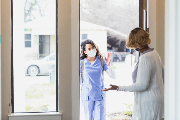 Senior woman welcomes home healthcare nurse into her home A female home healthcare nurse waves a greeting as she is welcomed into a patient's home. An elderly senior female patient is greeting the nurse at the front door. home caregiver stock pictures, royalty-free photos & images