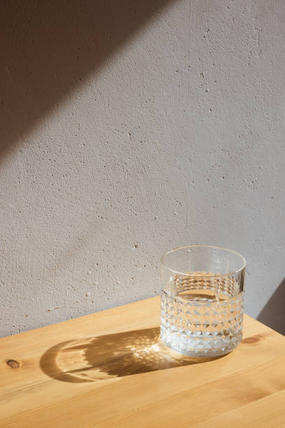 istock A glass with clean clear water and sharp shadows stands on a wood table on gray wall background 1314077712