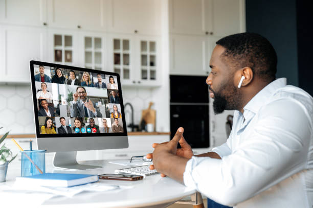istock Distance learning, online business briefing. Successful African American man uses computer for a video call, virtual meeting with partners, sits at workplace at home, multiracial people on the screen 1314079622