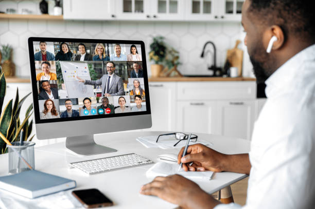 istock Online education, e-learning. African American smart confident guy sitting at home at work desk, uses computer, listening to an online lecture, taking notes, a teacher and diverse people on the screen 1314079623