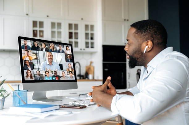 istock Distance learning, online business briefing. Successful African American man uses computer for a video call, virtual meeting with partners, sits at workplace at home, multiracial people on the screen 1314079631