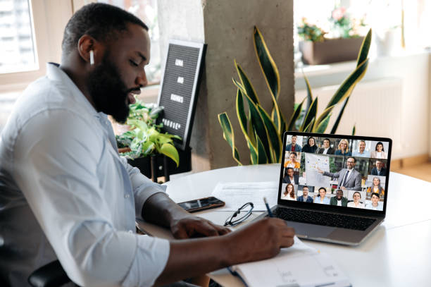 istock Online education, e-learning. Smart african american guy sits at the table at home, listens to an online lecture by laptop, makes notes, on the screen tutor and students, learning during quarantine 1314079639
